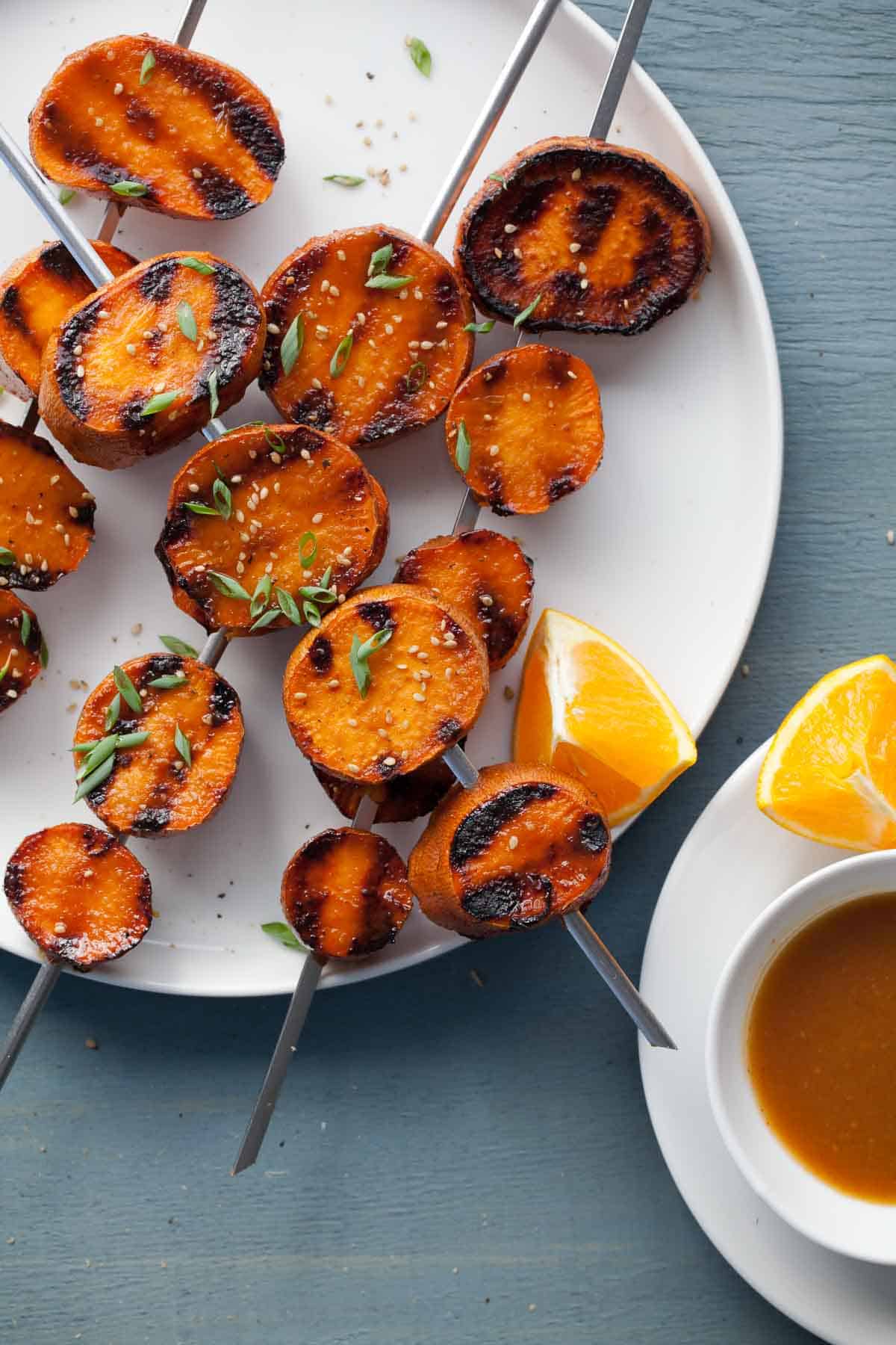 Miso-Orange Glazed Sweet Potatoes Skewers on Plate with Orange Wedges