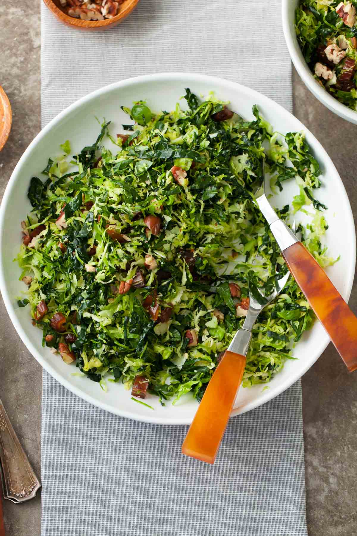 Shredded Brussels Sprout and Kale Salad in Large White Serving Dish with Spoons