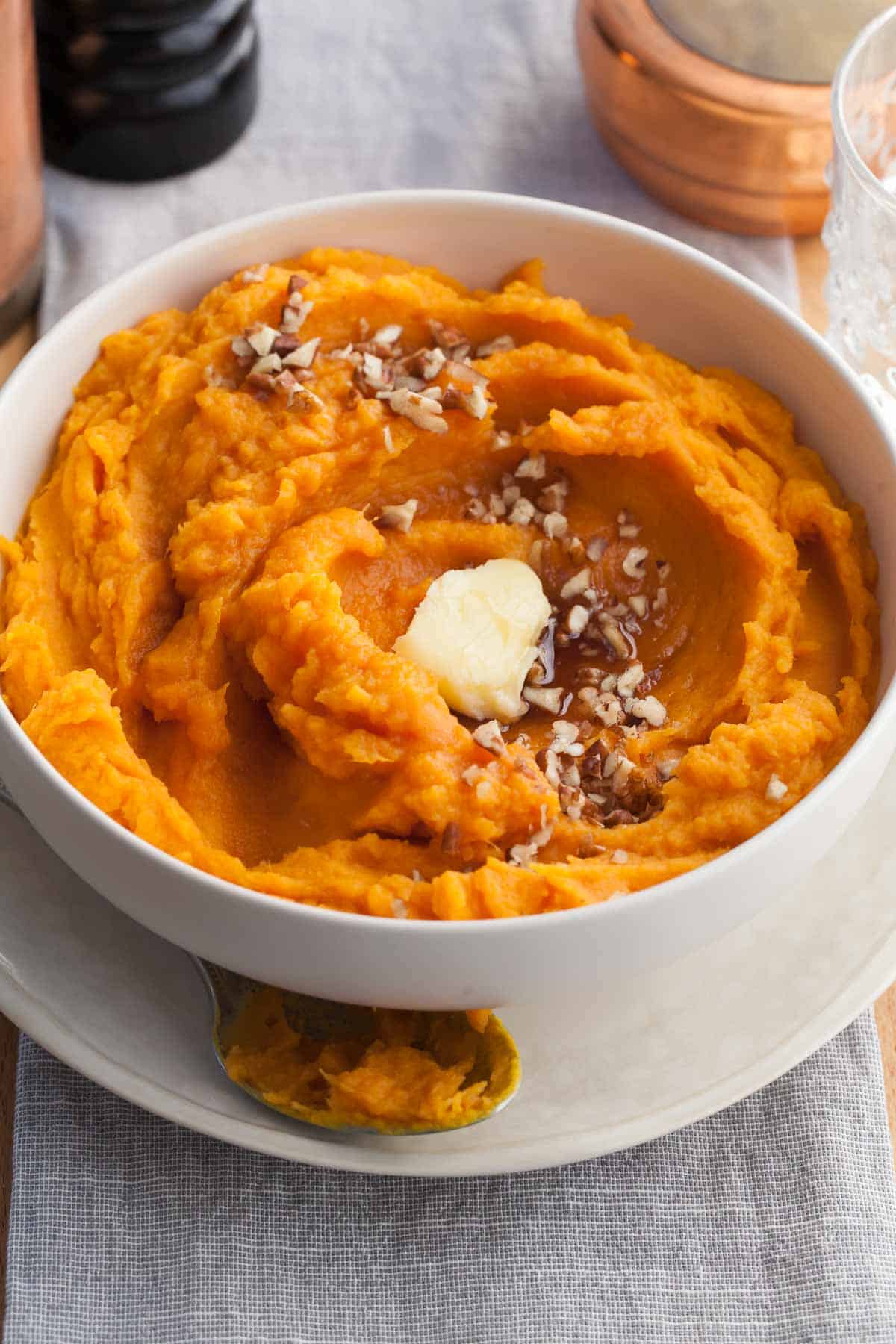 Steamed sweet potatoes mashed with vegan butter & maple syrup in serving bowl.