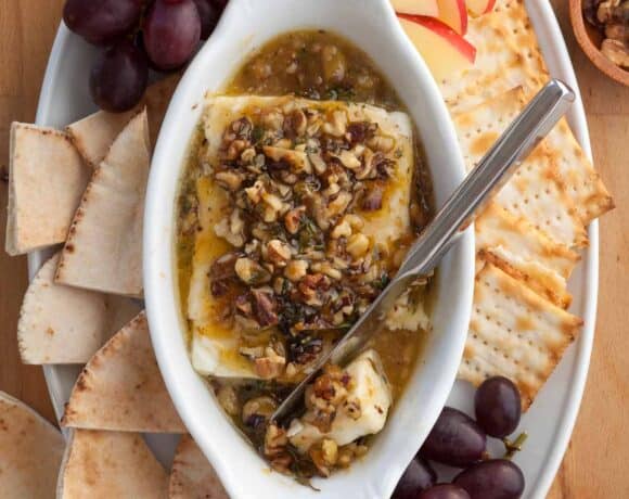 Baked Feta with Honey in dish with knife surrounded by bread and crackers.