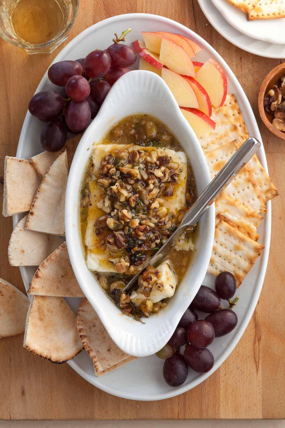Baked Feta with Honey in dish with knife surrounded by bread and crackers.