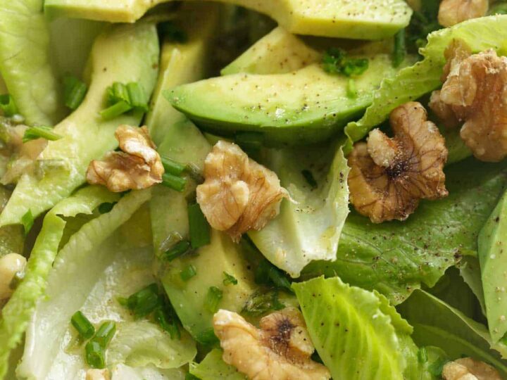 Close-up of romaine and avocado salad with sliced avocado, chopped chives, and toasted walnuts tossed in Dijon mustard vinaigrette.