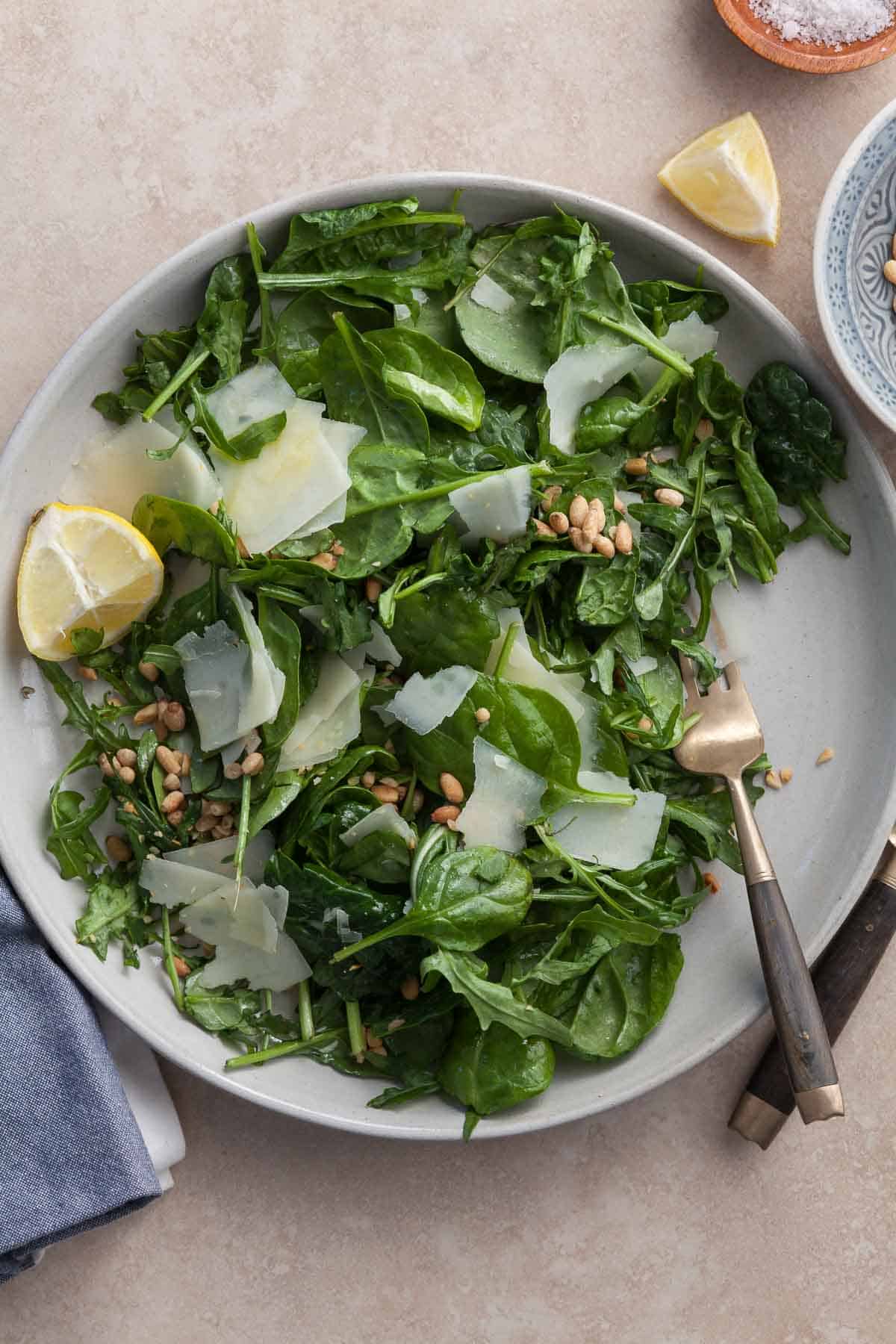 spinach and arugula salad with lemon dressing, pecorino and pine nuts on plate with fork