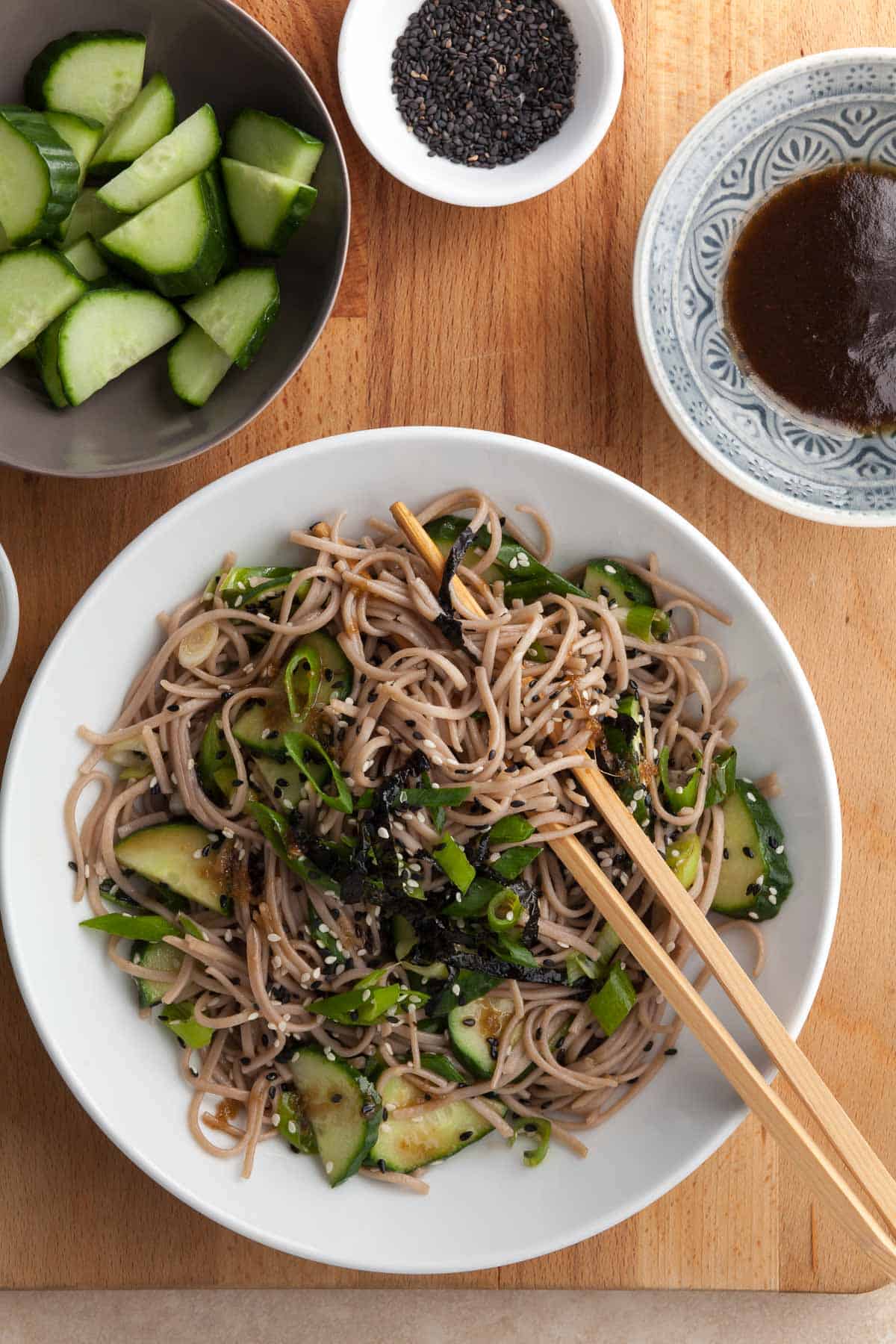 sesame soba noodles in bowl tossed in a sesame dressing and topped with scallions and sesame seeds served in bowl with chopsticks