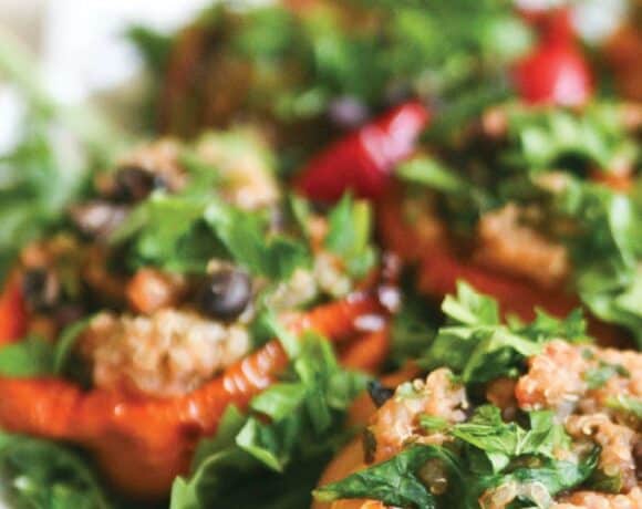 Vegetarian quinoa stuffed peppers served over arugula with lemon and parsley garnish
