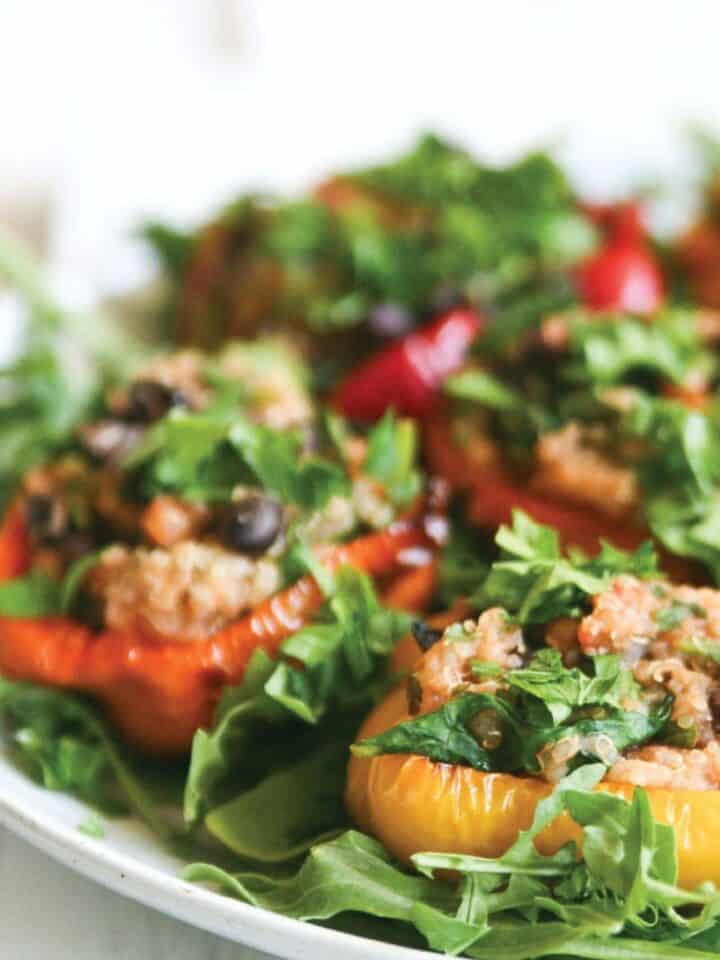 Vegetarian quinoa stuffed peppers served over arugula with lemon and parsley garnish