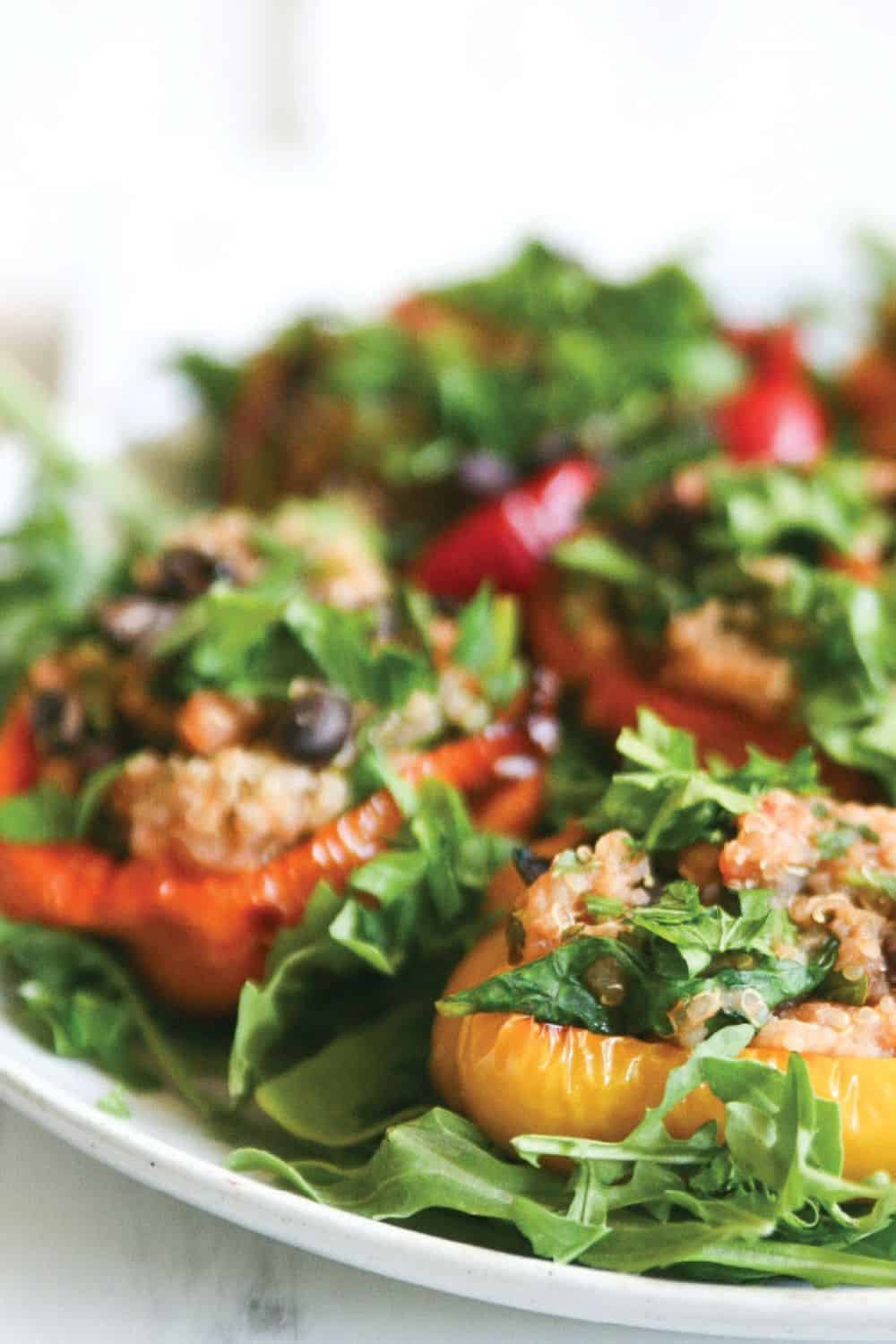 Vegetarian quinoa stuffed peppers served over arugula with lemon and parsley garnish