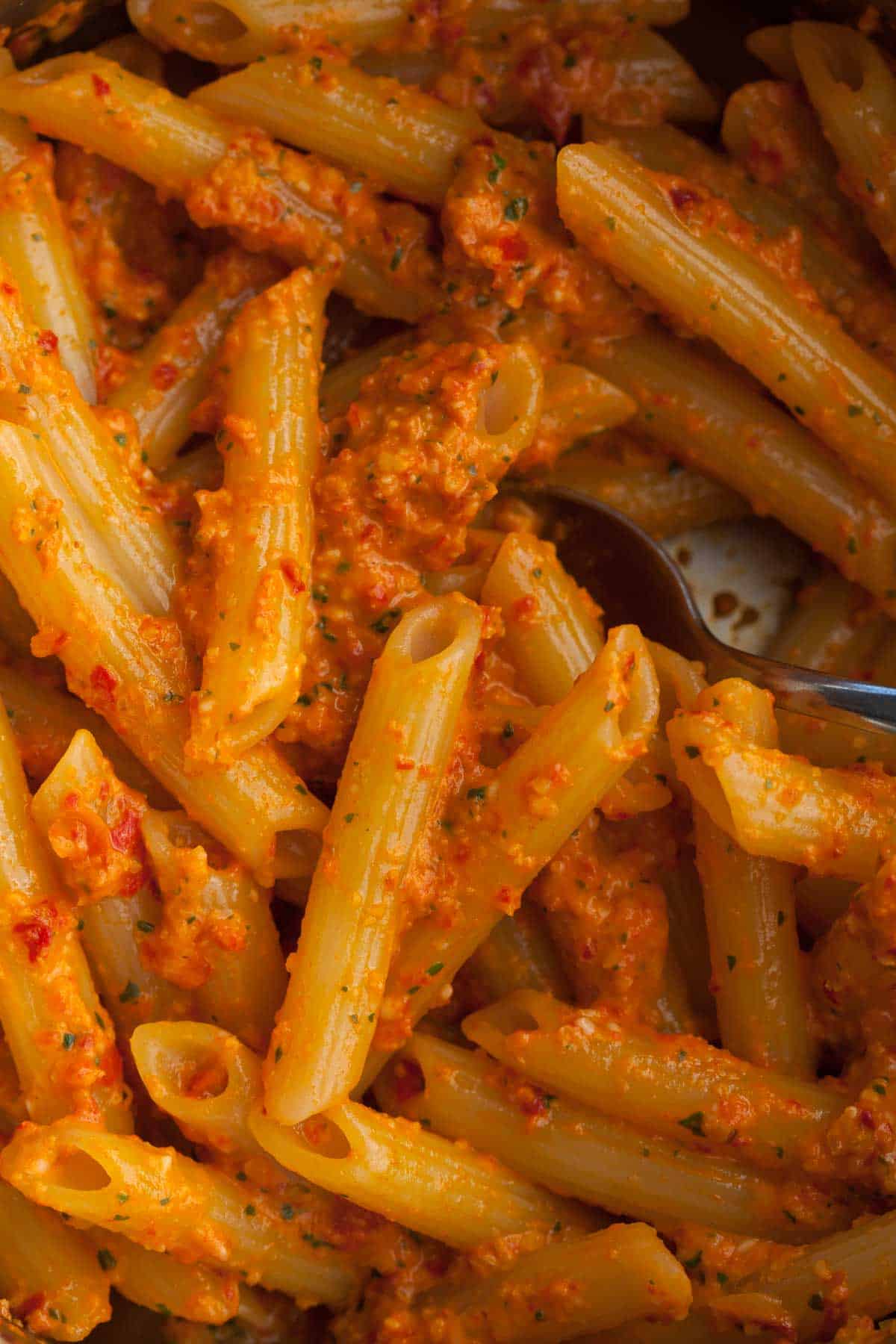 red pepper pesto tossed with pasta in pan close up