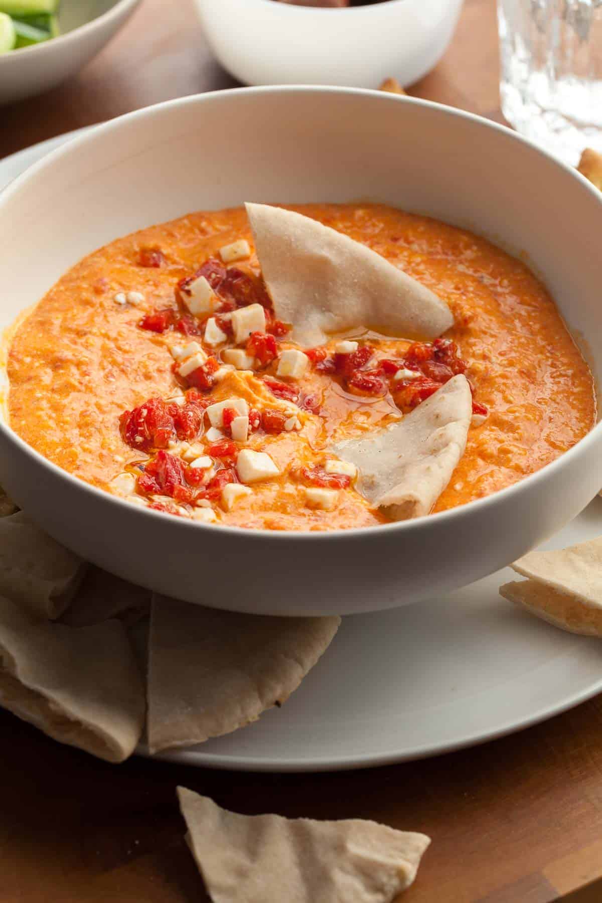 roasted red pepper and feta dip in bowl topped with chopped red peppers and feta
