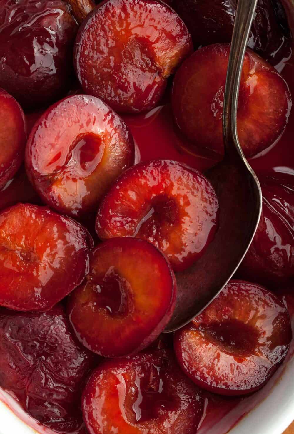 roasted plums in syrup with spoon close up