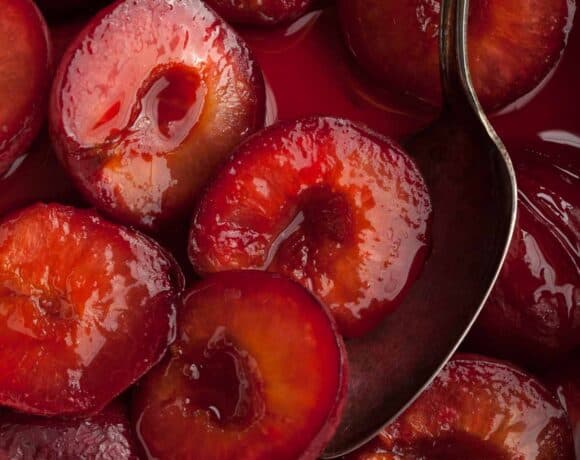 roasted plums in syrup with spoon close up