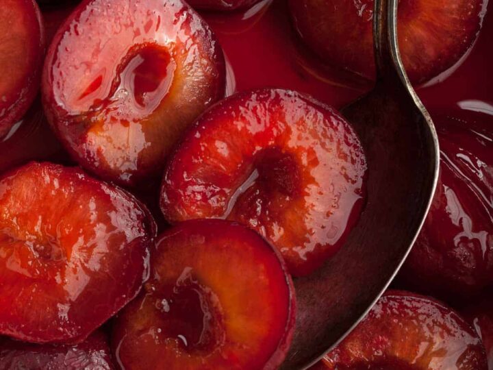 roasted plums in syrup with spoon close up