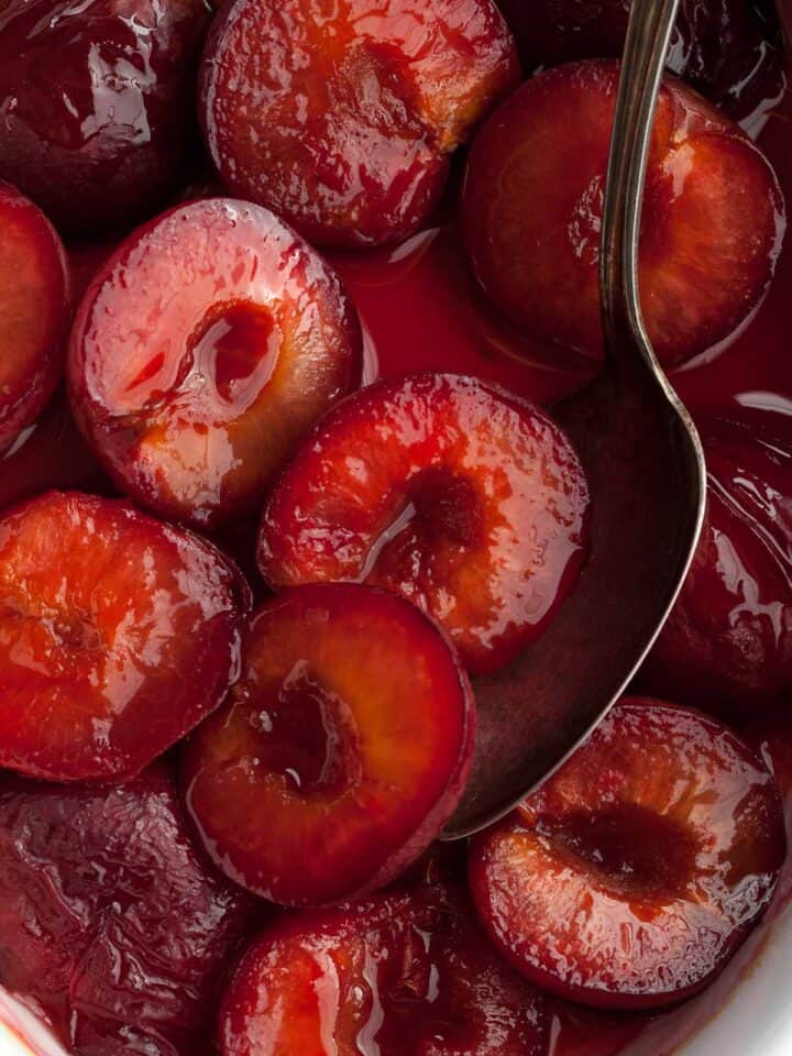 roasted plums in syrup with spoon close up