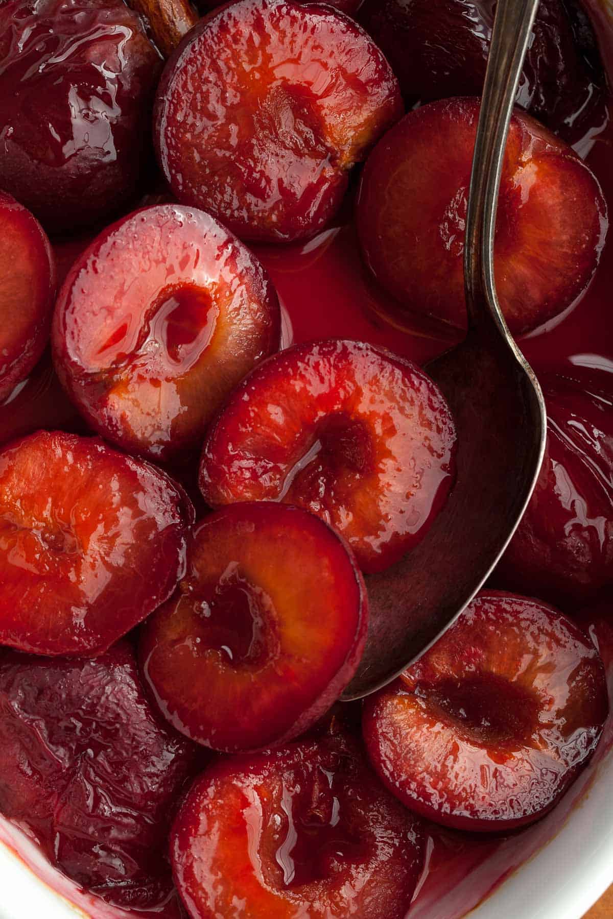 roasted plums in syrup with spoon close up
