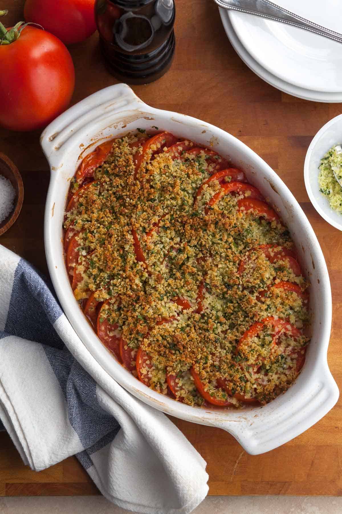 tomato gratin with slices of tomatoes topped with cheese and herbs on wooden board